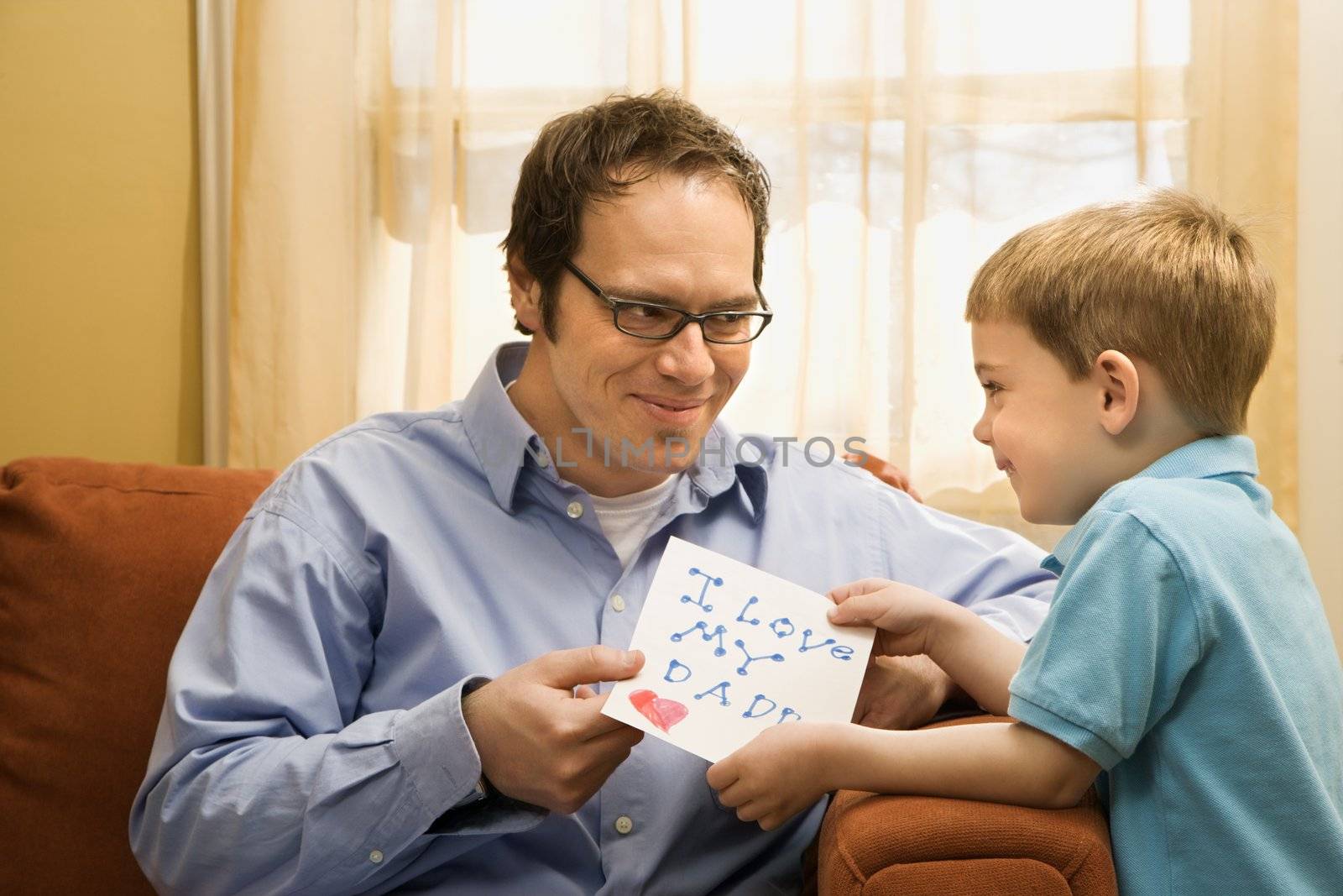 Caucasian boy giving mid adult father a drawing.