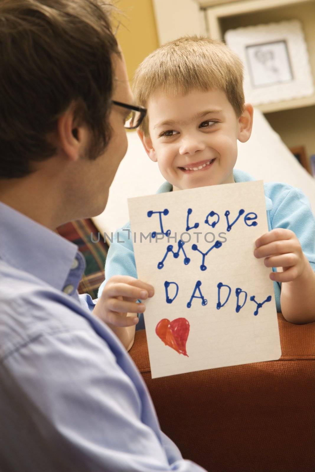 Caucasian boy giving mid adult father a drawing.