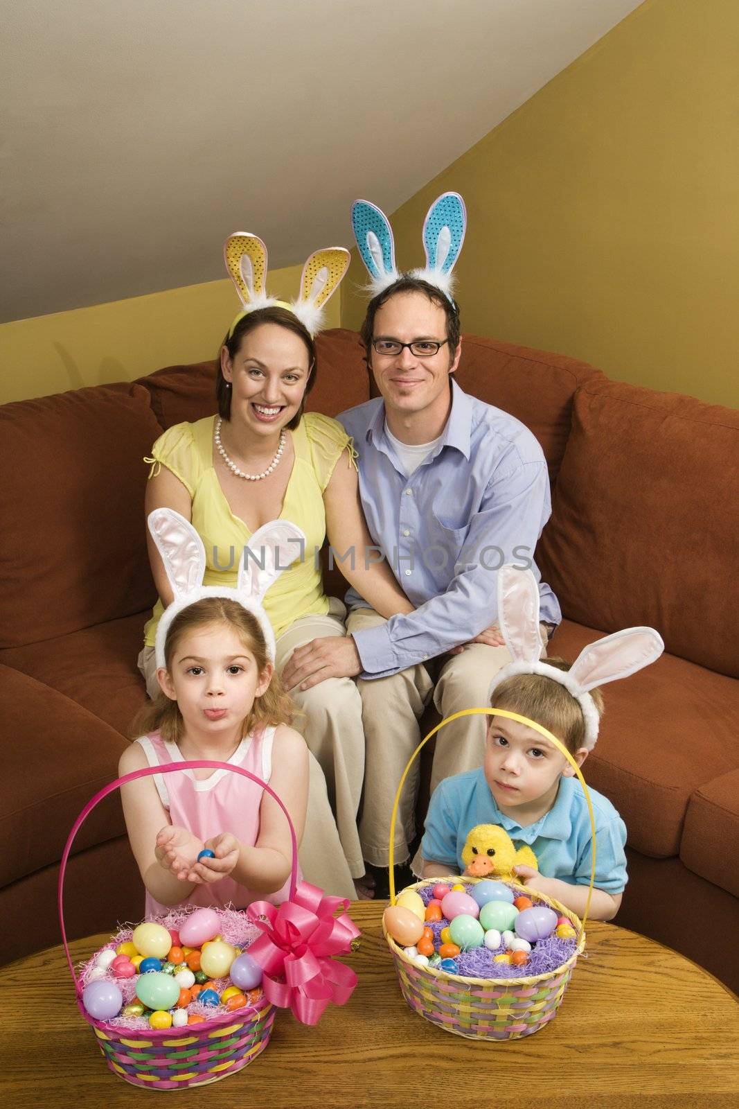 Caucasian family wearing rabbit ears with Easter baskets looking at viewer.