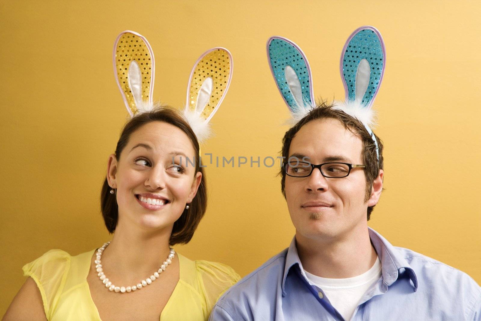 Caucasian mid adult couple wearing rabbit ears and looking at each other.