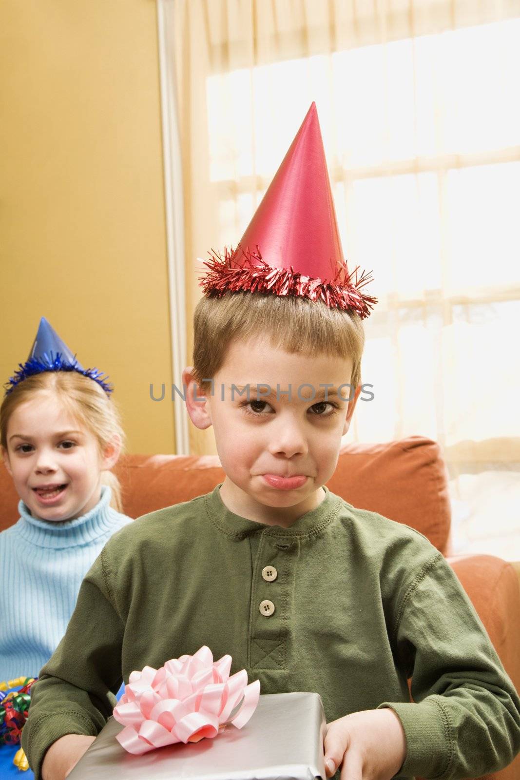 Caucasian boy wearing party hat pouting and looking at viewer.