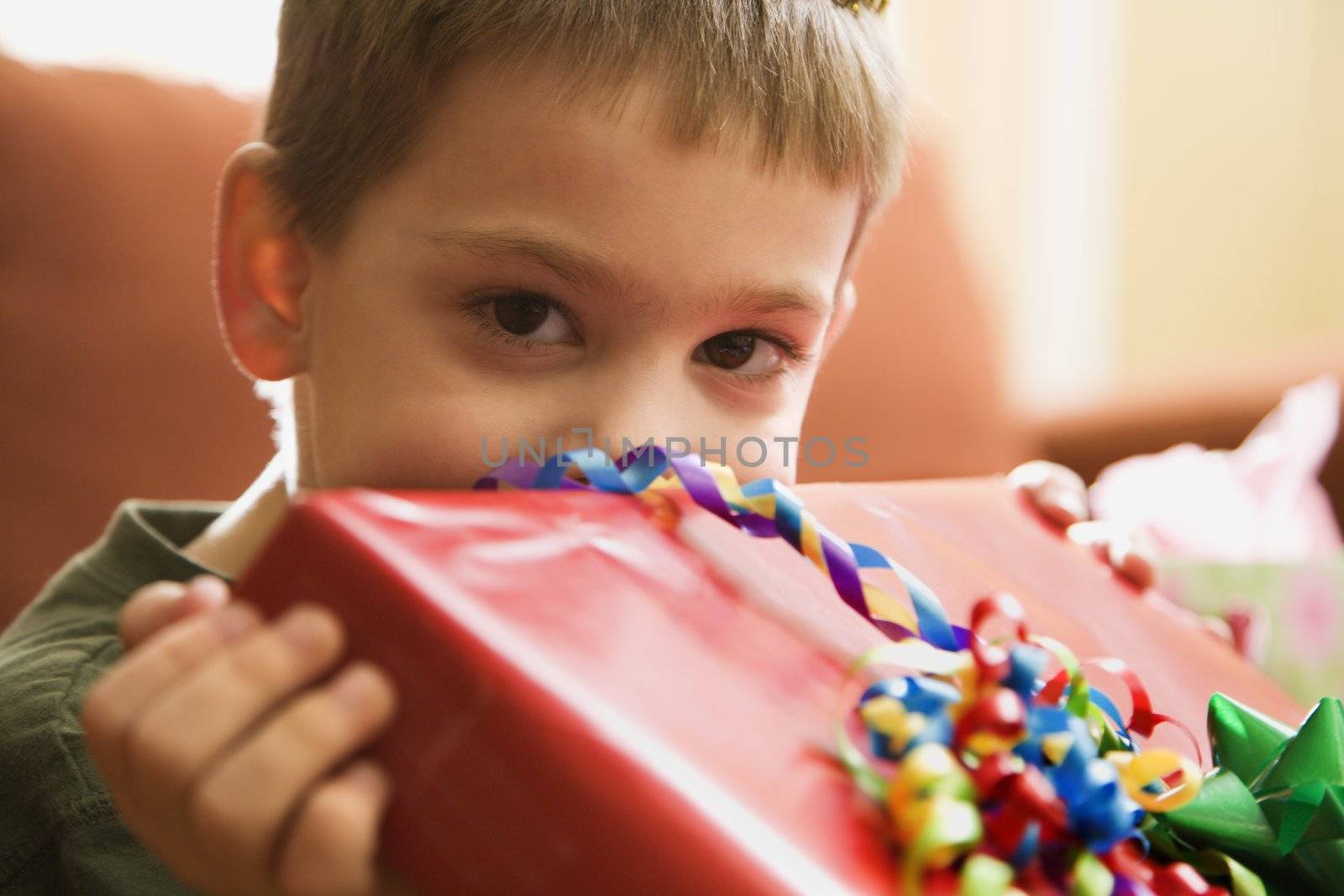 Caucasian boy holding gift up to face and looking at viewer.