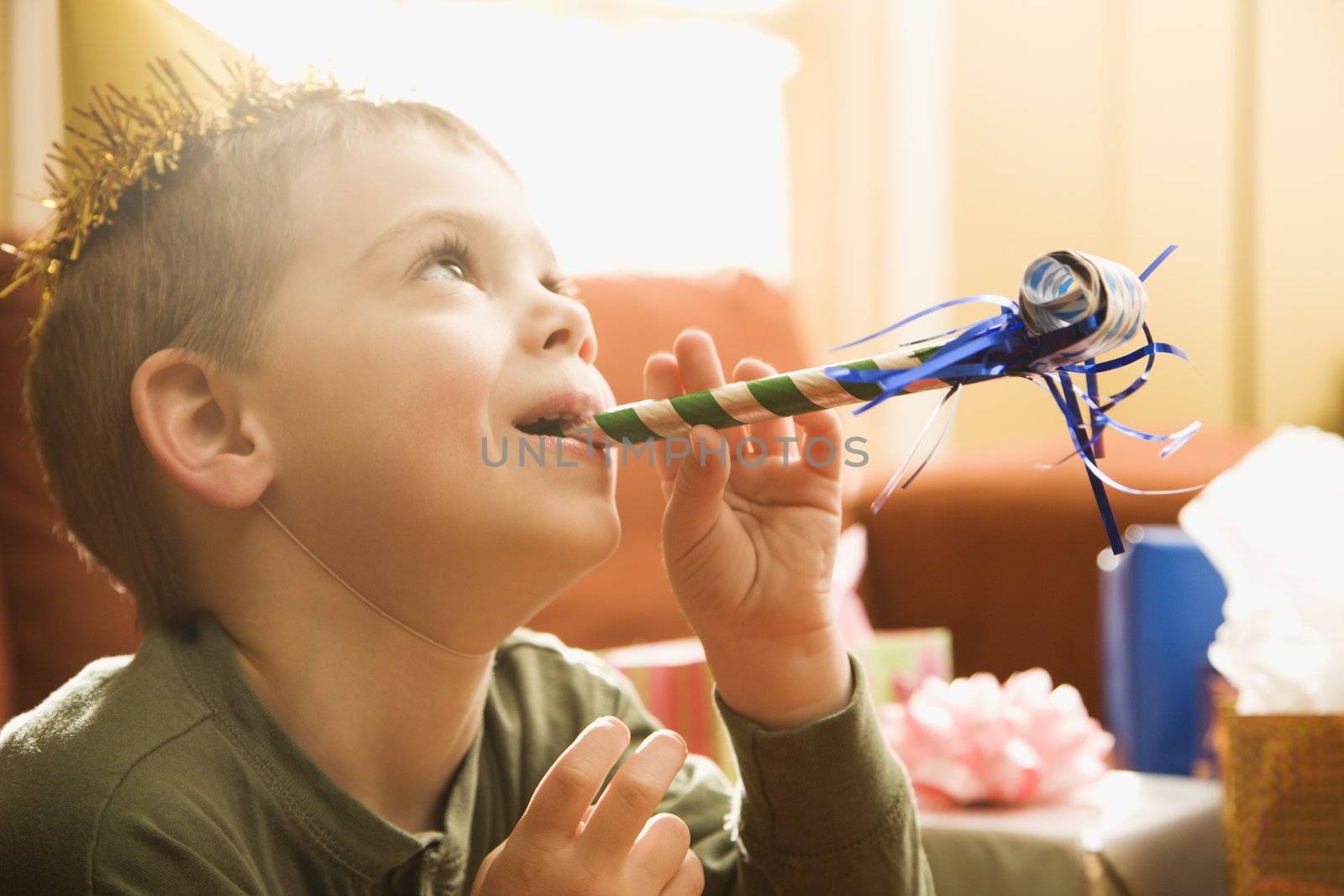 Caucasian boy at birthday party blowing noisemaker.