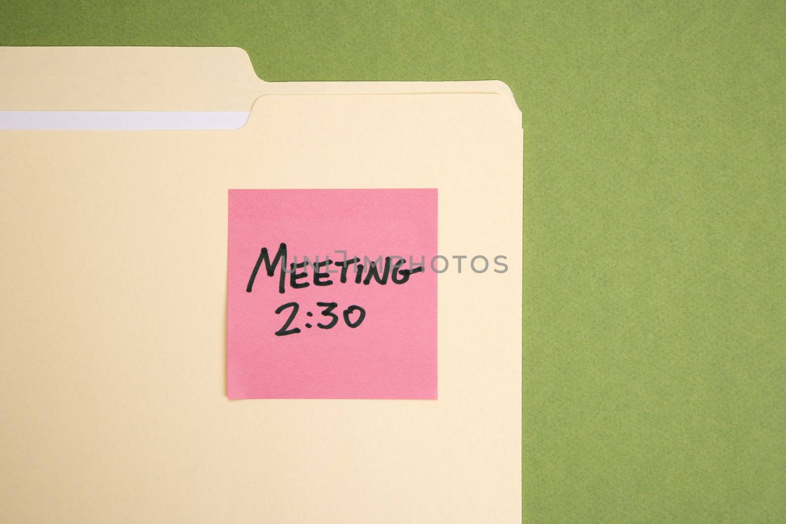 Folder with pink sticky note reminder for a meeting on a green background.