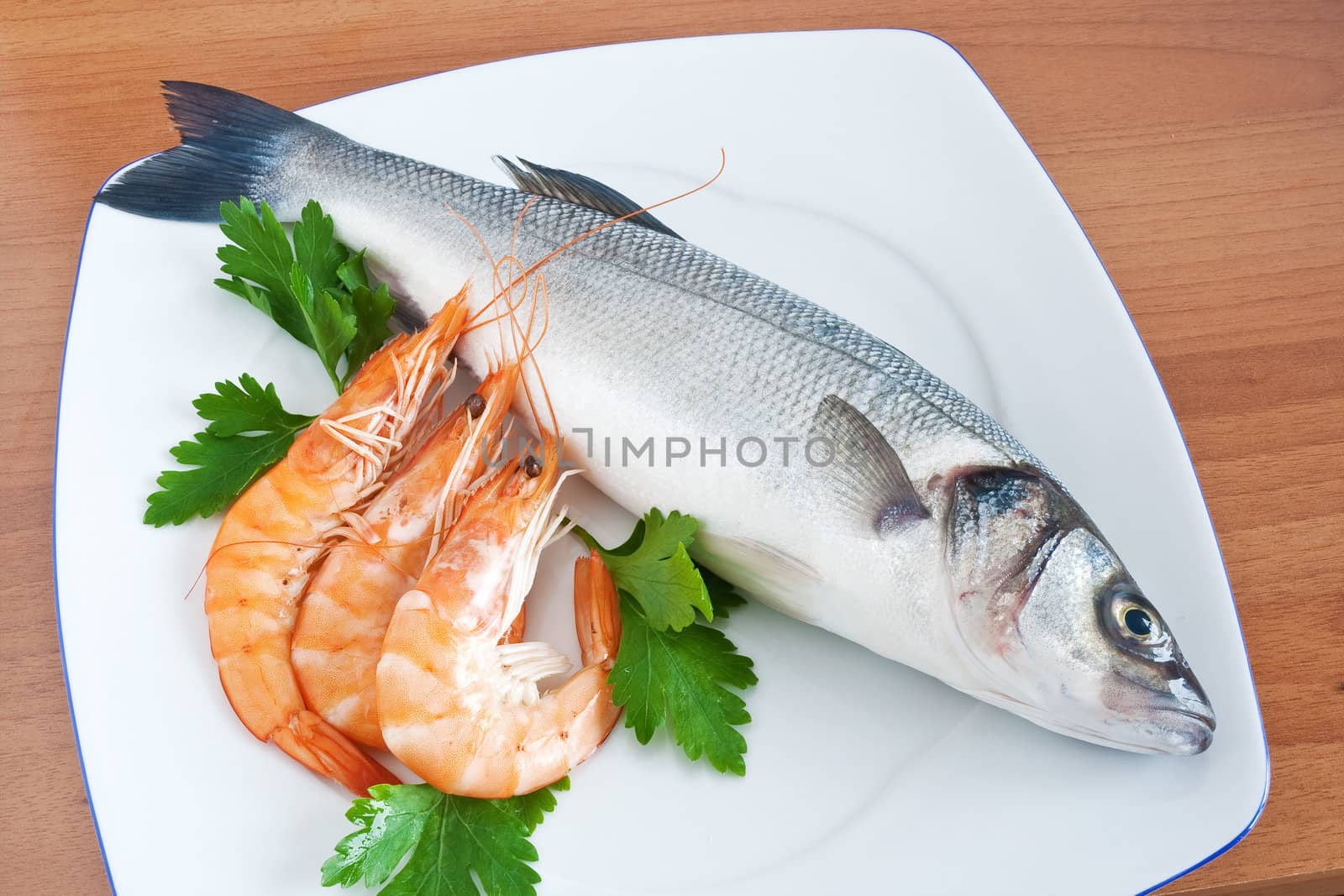 plate with sea bass, prawns, and parsley isolated on wooden background