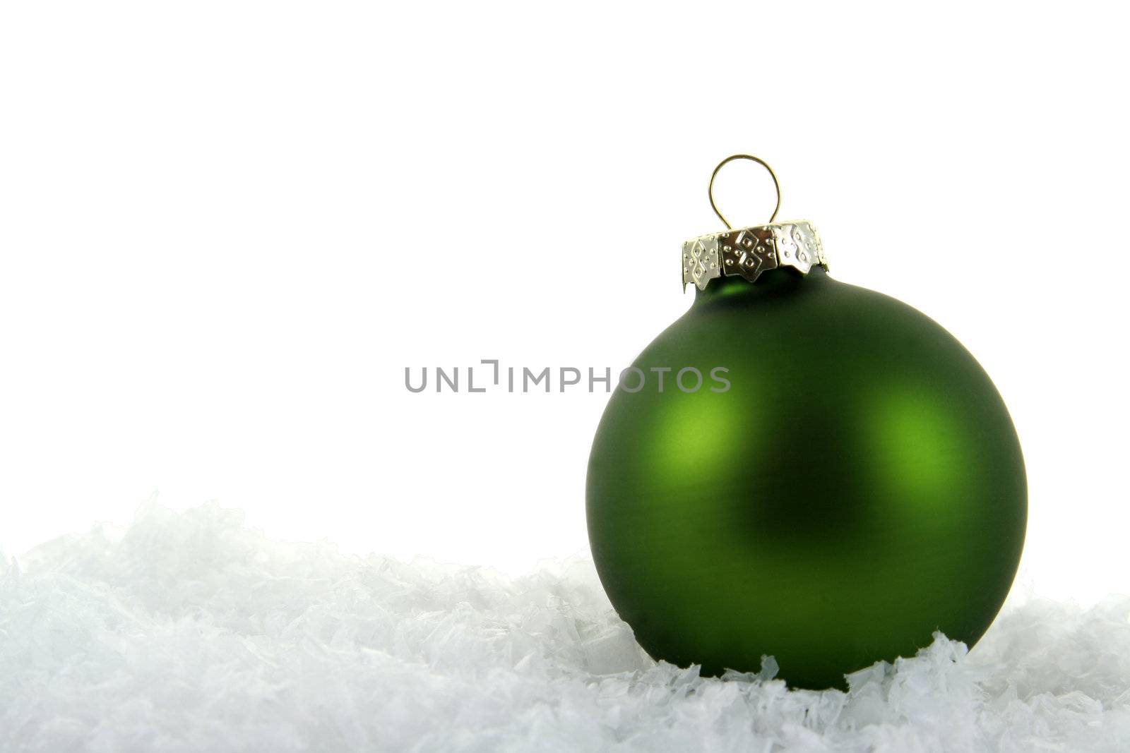 A green Christmas bauble sitting in a bed of snow.
