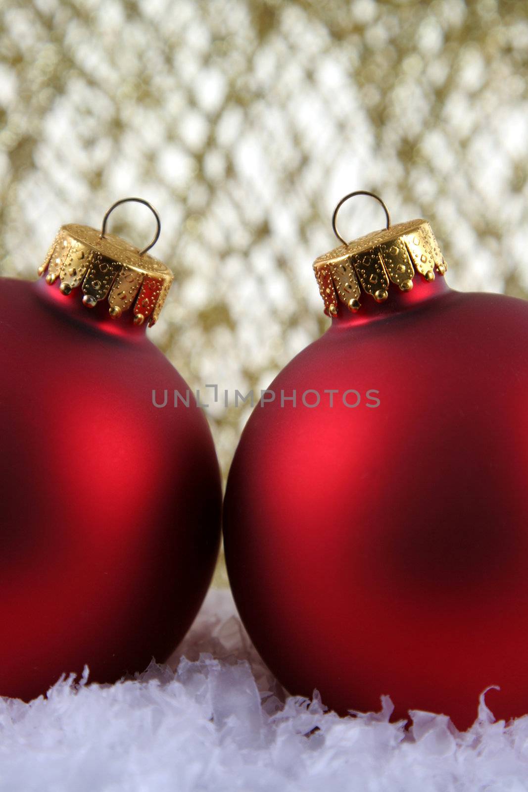 Two red Christmas bauble backed by gold glittery strings.
