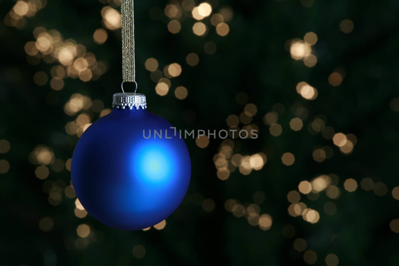 Blue Christmas ornament hanging against lit Christmas tree