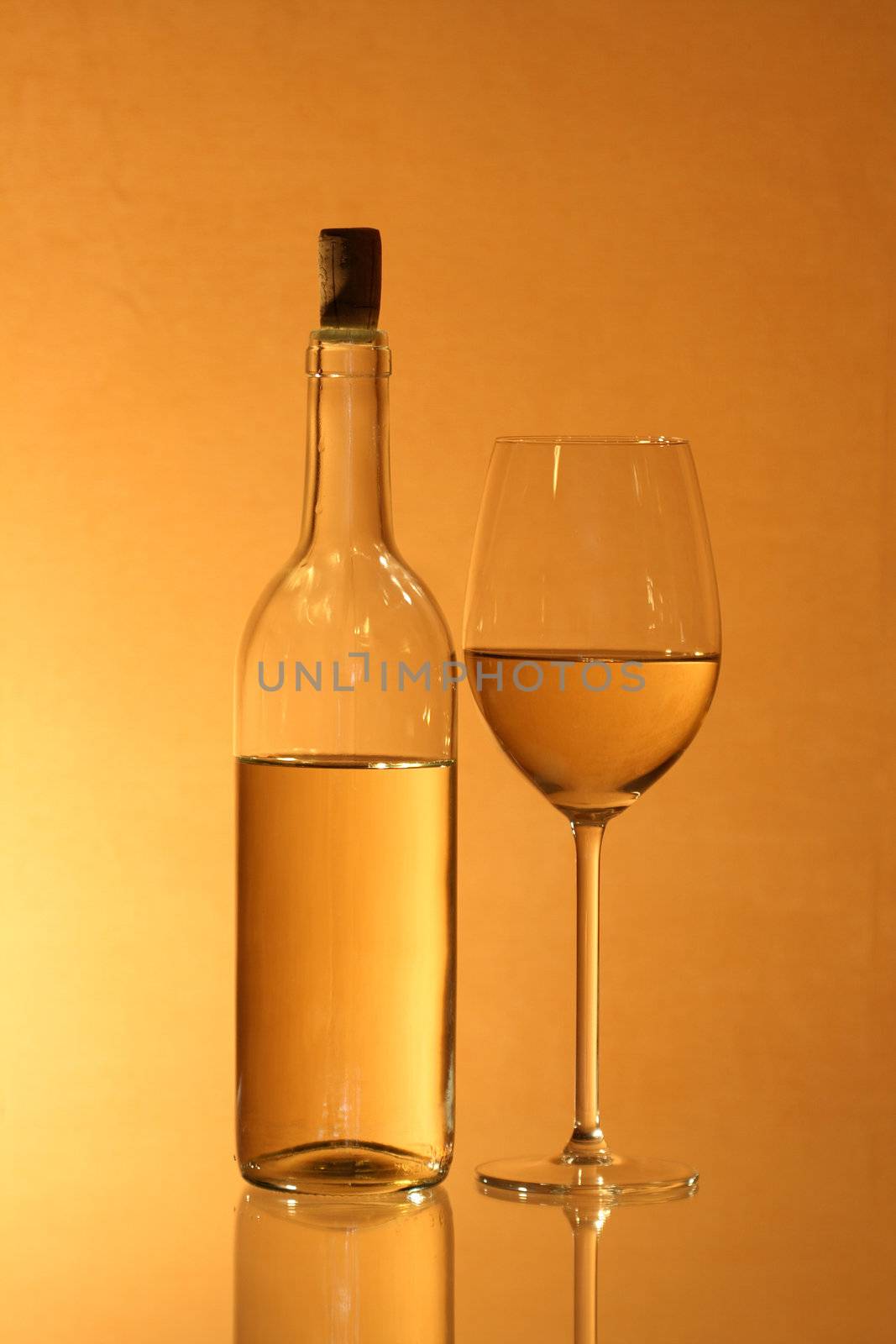 Wineglass near bottle of white wine with reverberation on red-yellow background