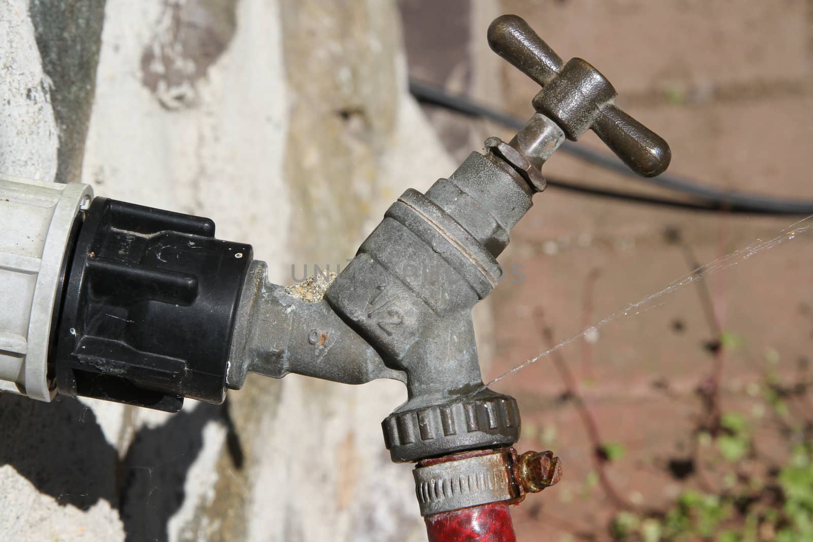 Old tap with hose attached, water spraying out from a leak,