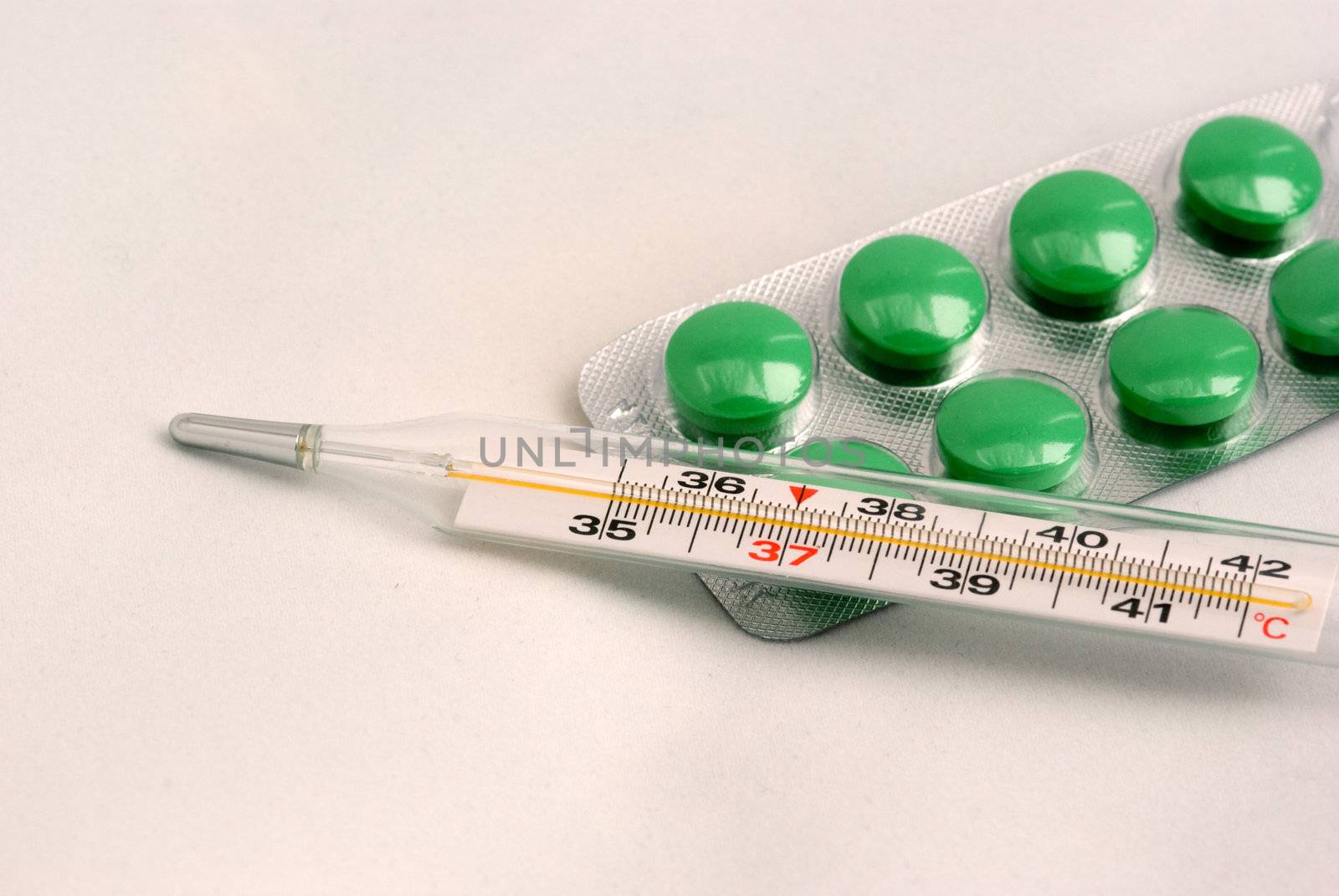 The medical thermometer and green tablets on a light grey background