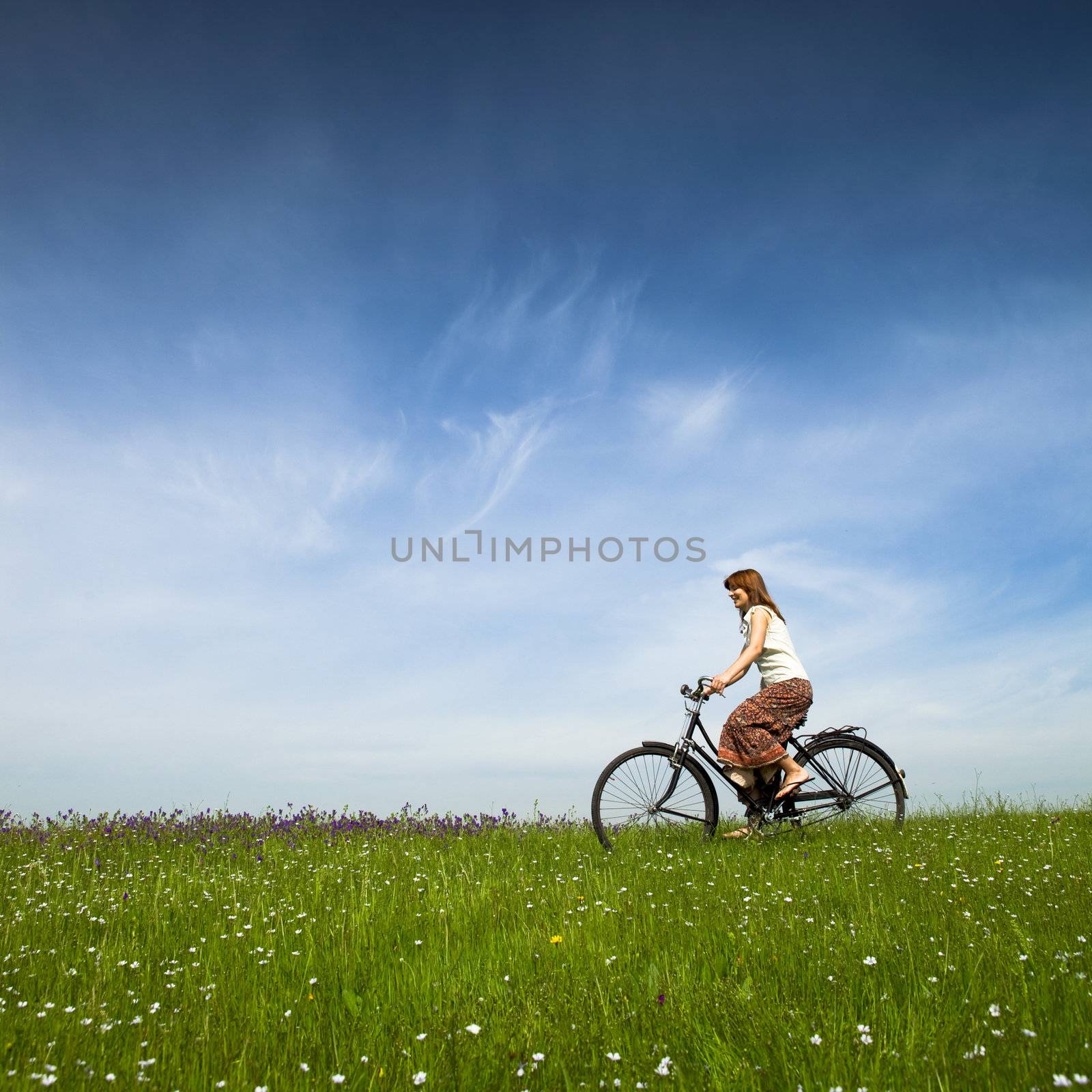 Happy young woman on a green meadow riding a bicycle