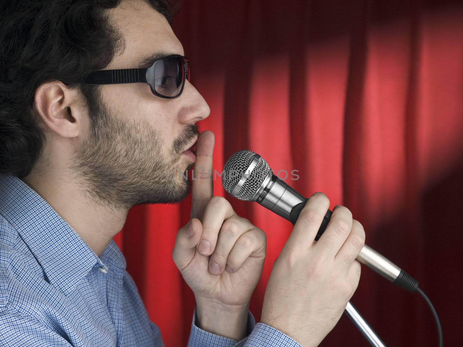 A young man with sunglasses hushing the audience on the mic.