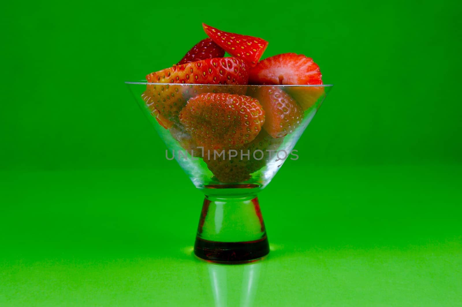 Strawberries in a cocktail glass islolated against a green background