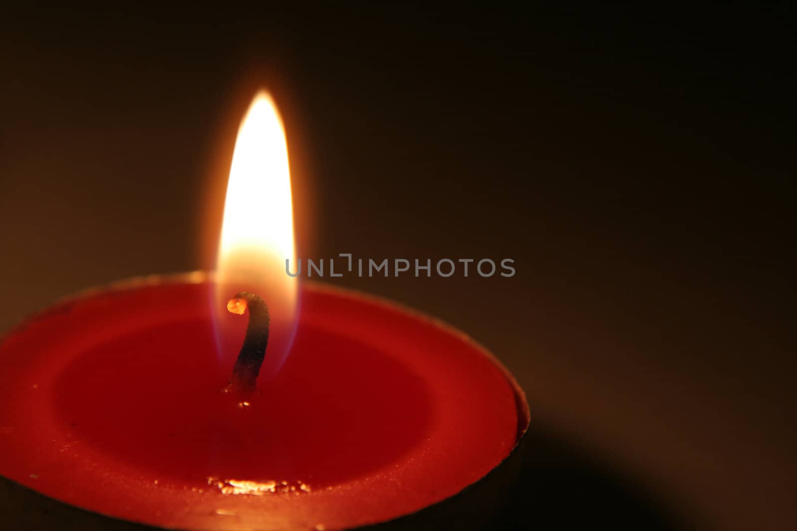 A single lit red Christmas tea light.
