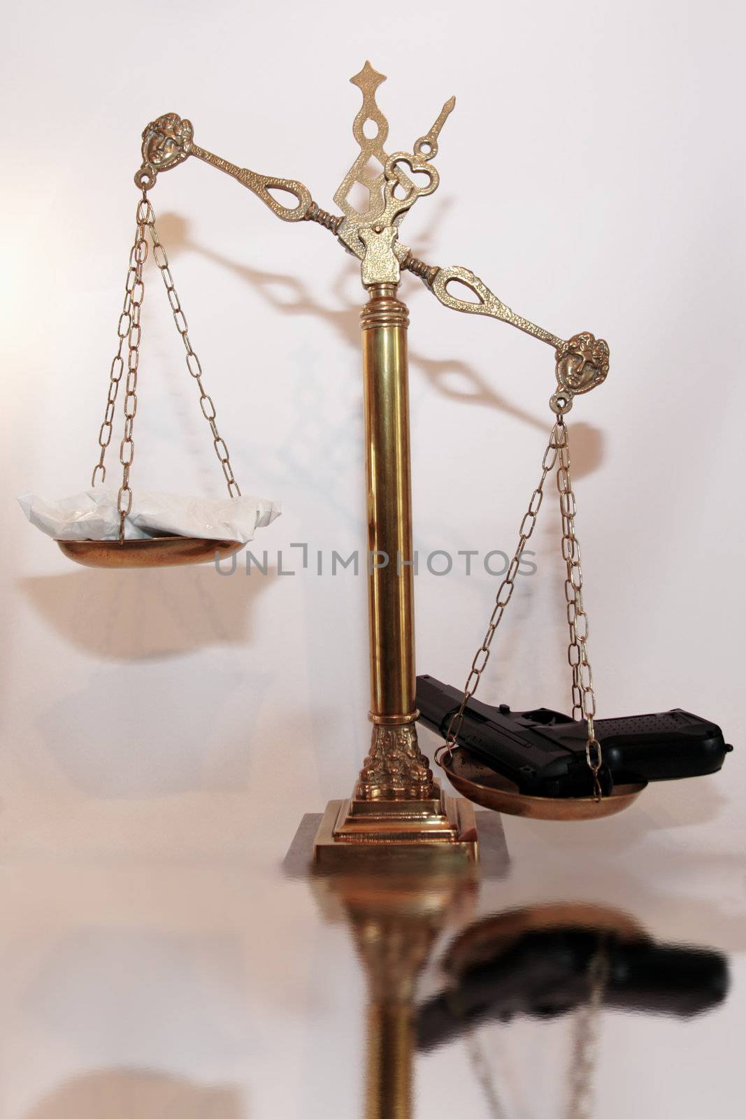 an antique scales against a white background with drugs and gun depicting drug crime