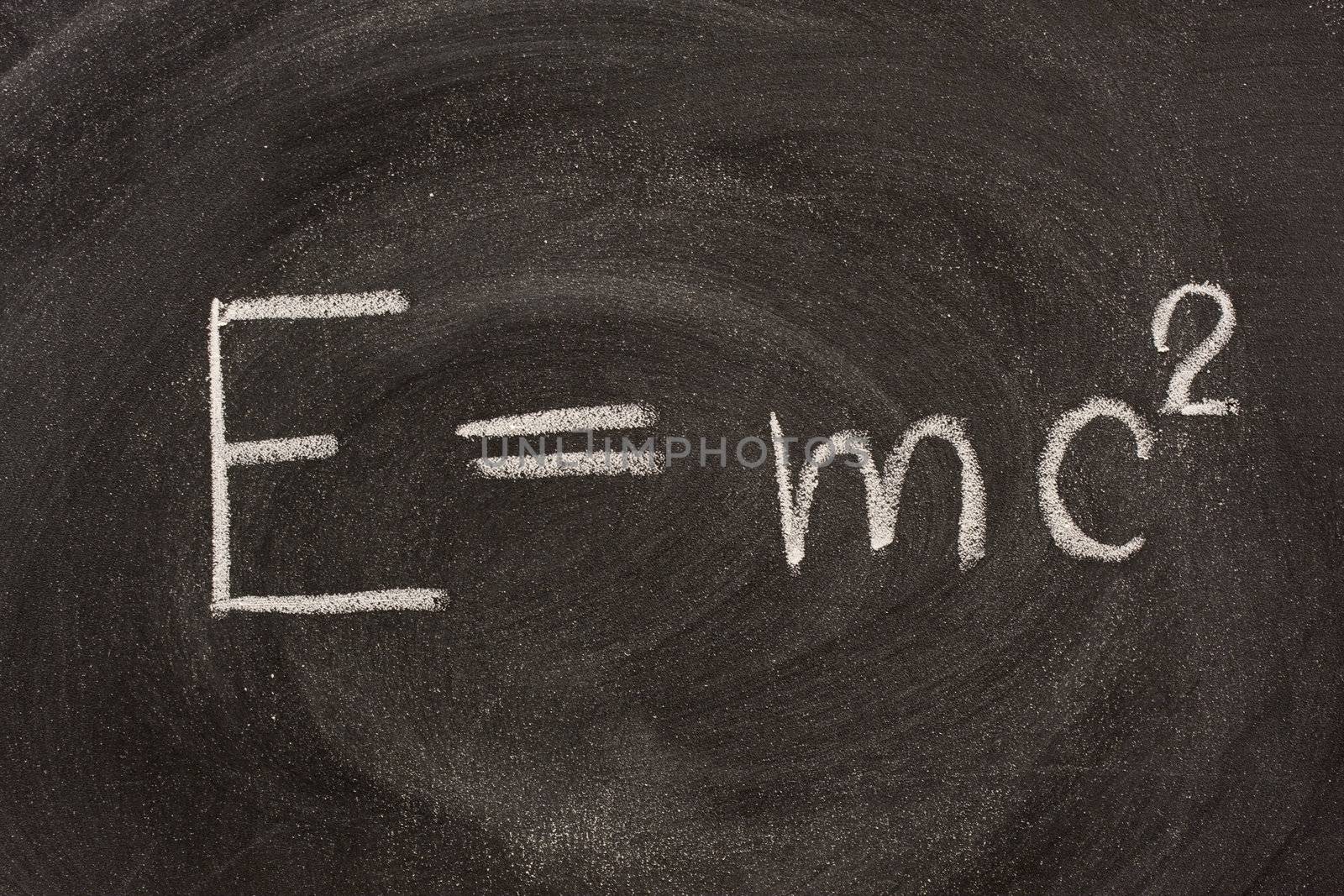 Albert Einstein well known physical formula, E=mc2, describing equivalence of matter mass (m) and energy (E) with including speed of light.  It is hadwritten with white chalk on school blackboard with strong smudge patterns.