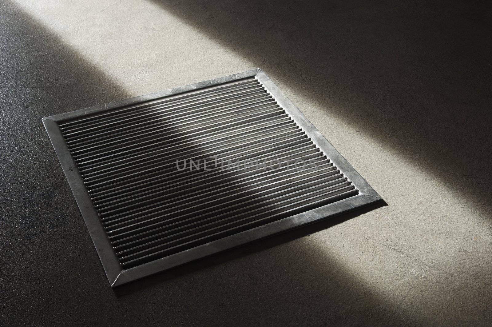 Steel grate in a concrete floor partially lit