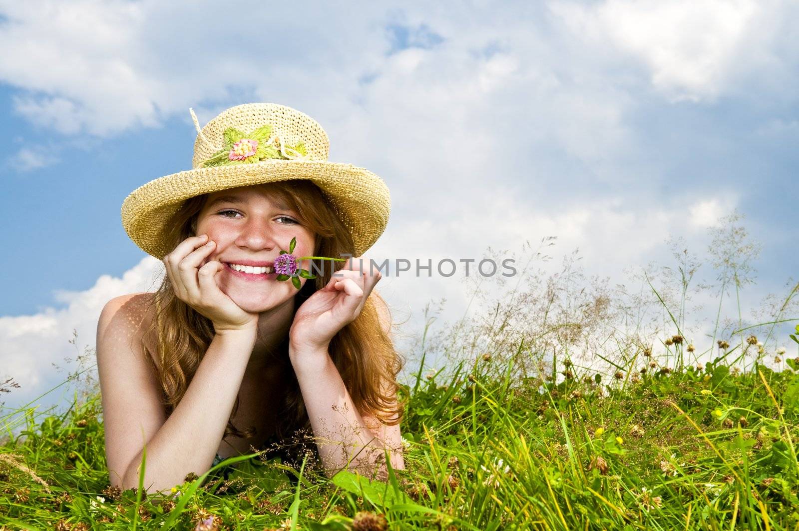 Young teenage girl laying in summer meadow resting chin on hand holding flower