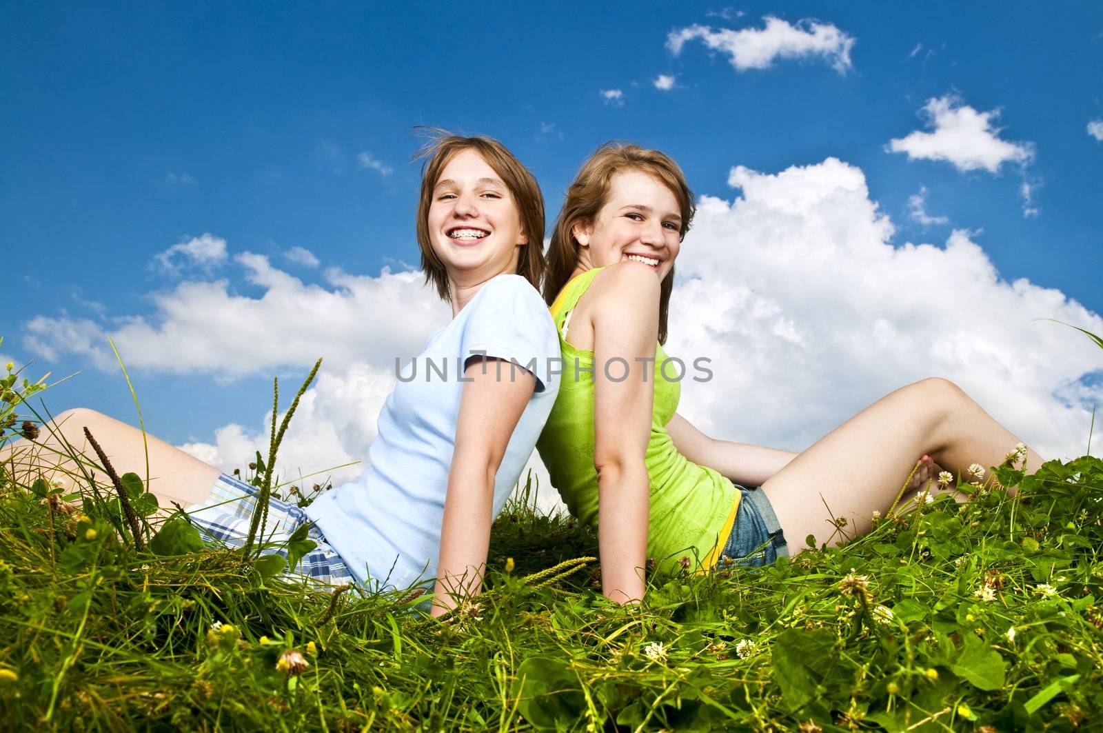 Young girls sitting in meadow by elenathewise