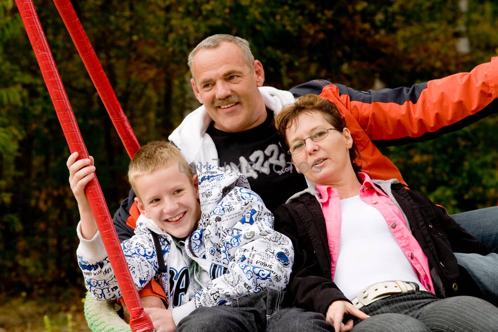 Happy young family in the swing on the playground