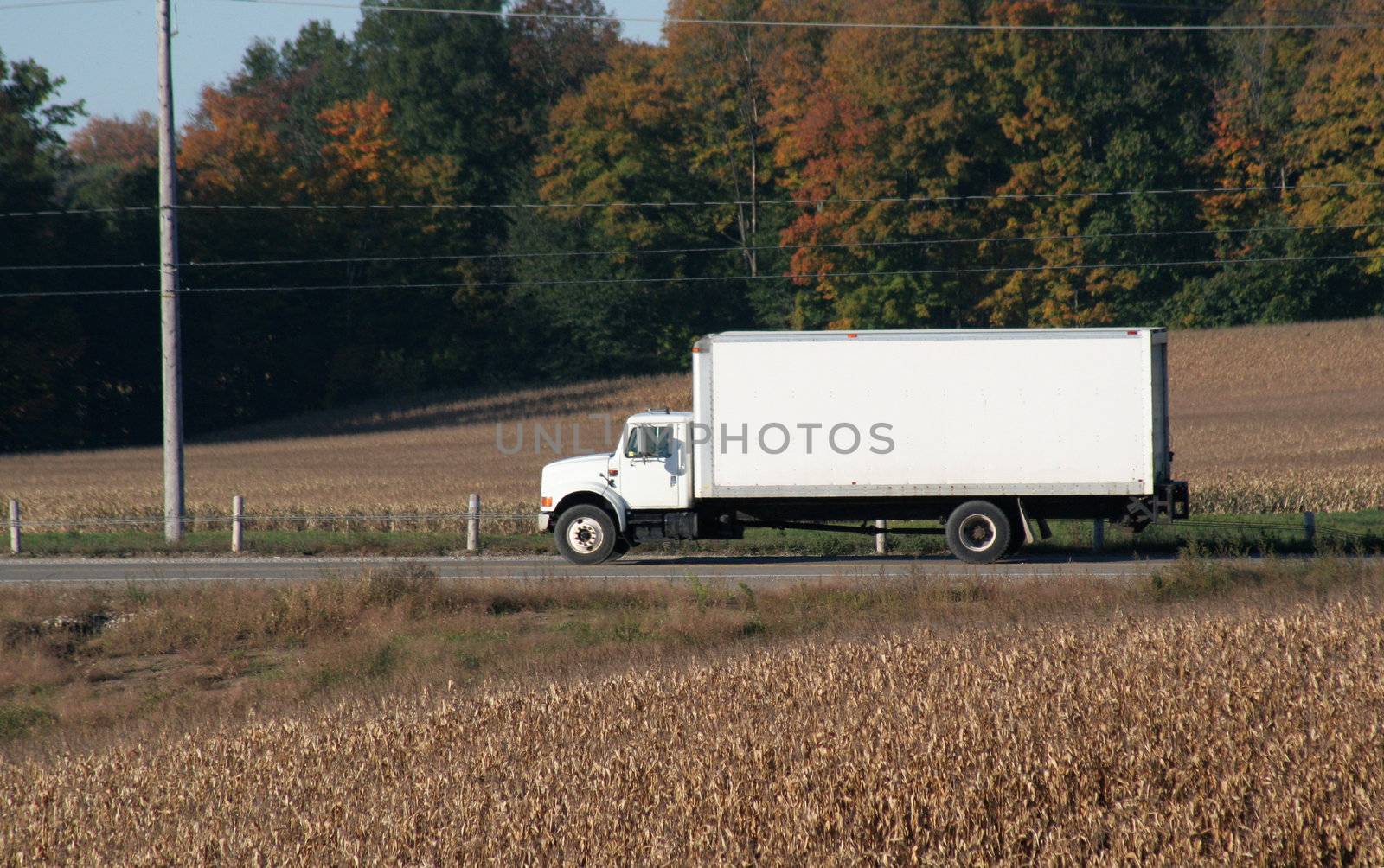 A plain white cube van speeding on a road during the harvest.