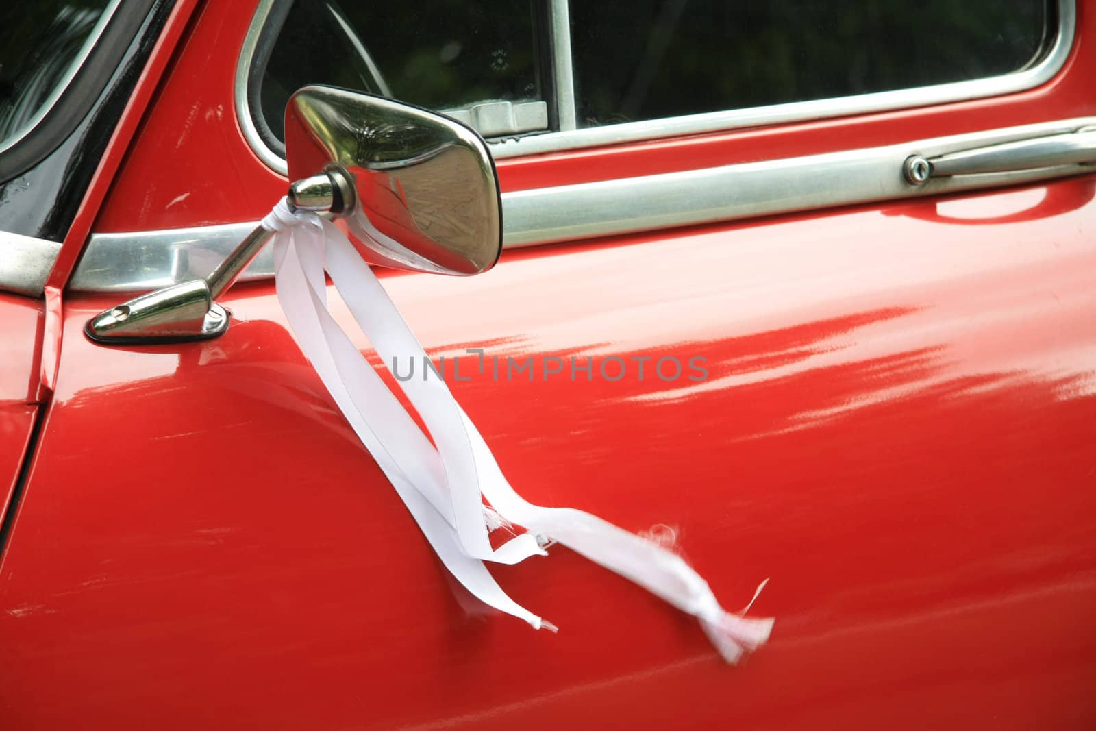 A vintage red car had a white ribbon on its mirror as a wedding decoration