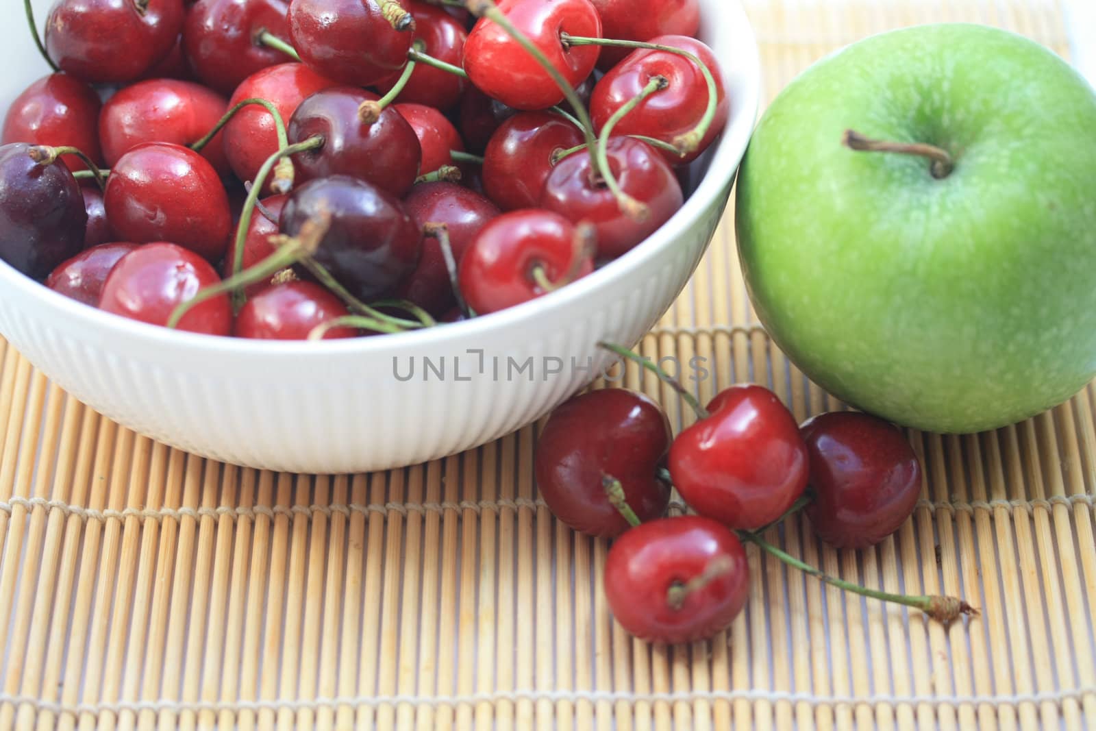 A group of juicy, fresh cherries in a white bowl and a green apple