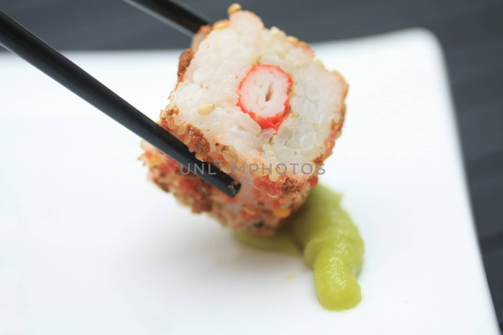 A piece of seame seed sushi and a pair of chopsticks