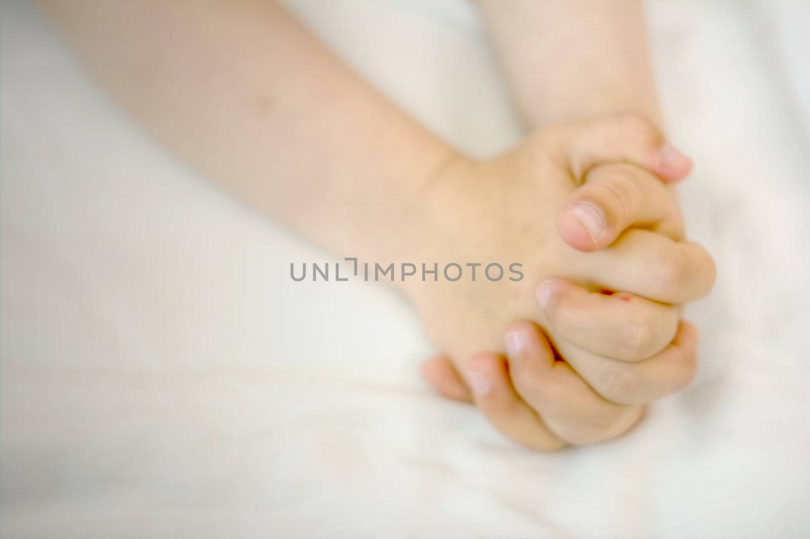 A child's hands folded in prayer on white cloth.