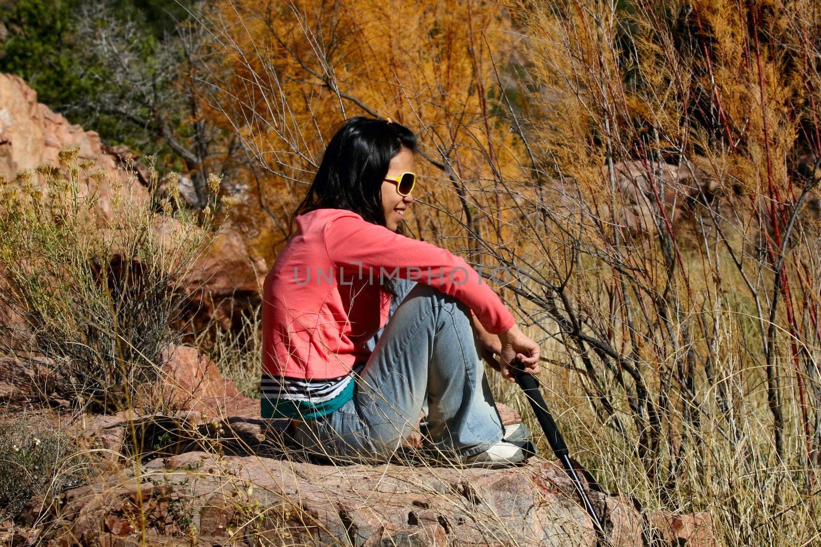 Beautiful young asian girl sitting on large rock in wilderness