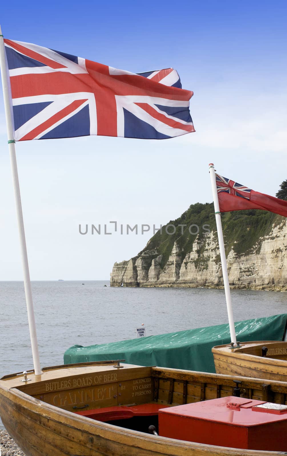 Wooden day trip boats flying the union jack flag, on the beach at Beer in Dorset England. Set against a coastal background.