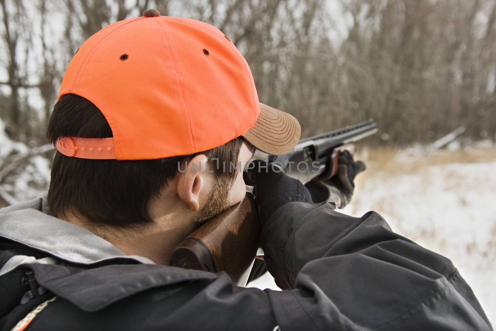 Caucasian male aiming shotgun out towards woods.