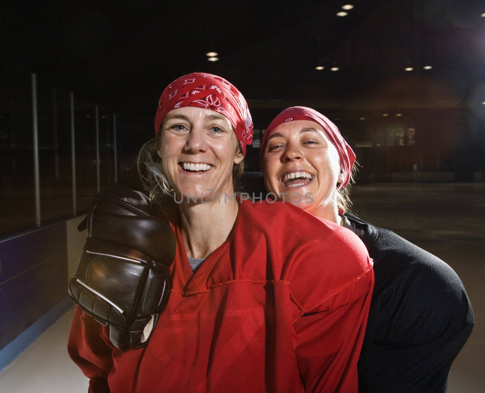 Women hockey players in uniform posing with helmets off on ice rink.