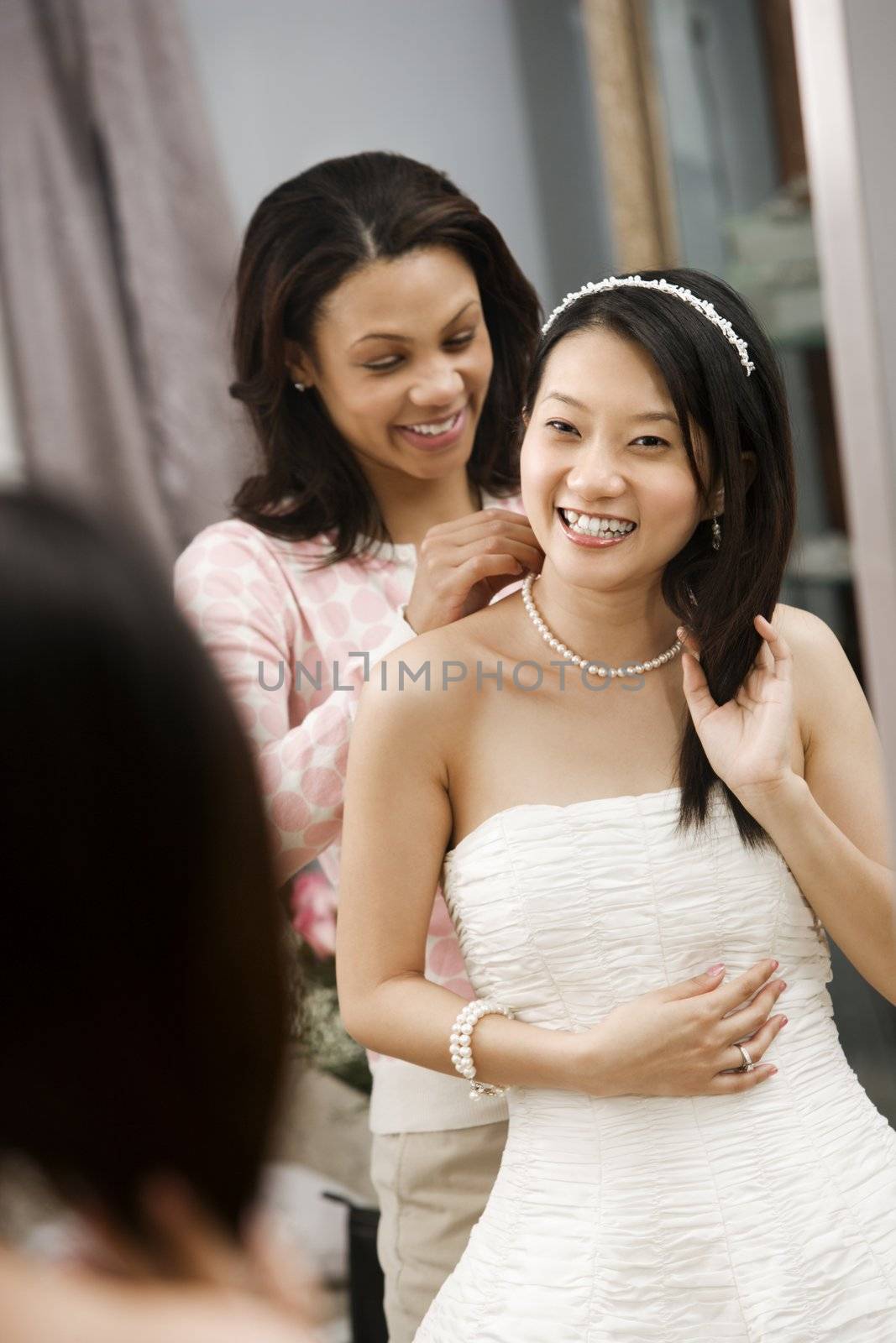 African-American friend helping place necklace on Asian bride.