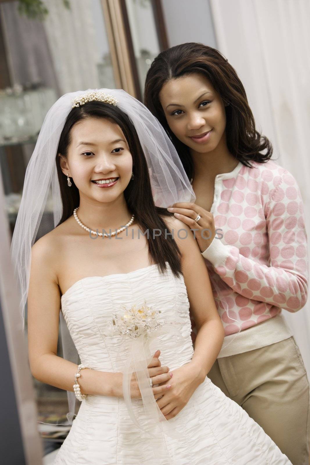 Asian bride and African-American friend admiring dress in mirror.