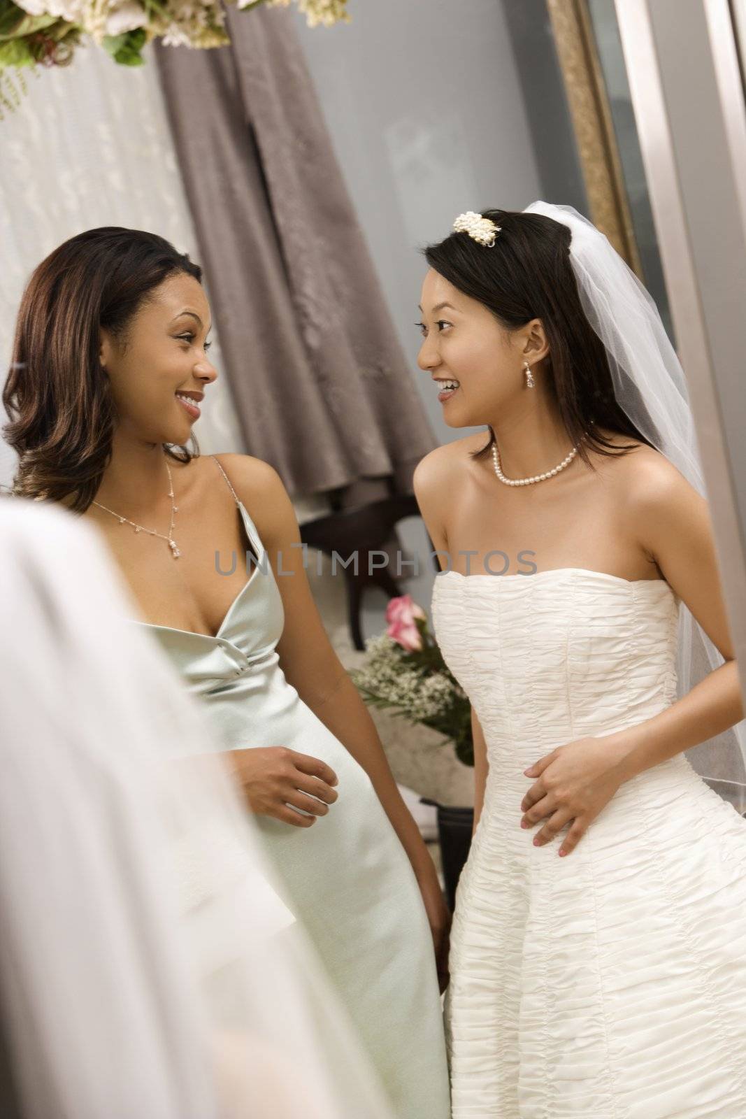 Asian bride and African-American bridesmaid talking to each other.