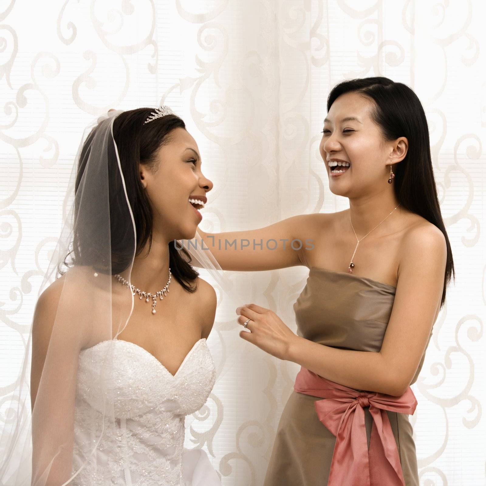 Asian bridesmaid laughing with African-American bride.