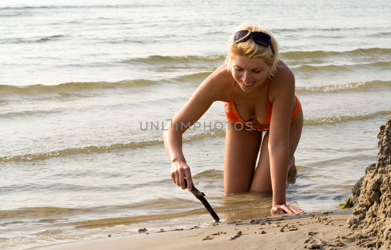 pretty blond in bikini drawing on the sand