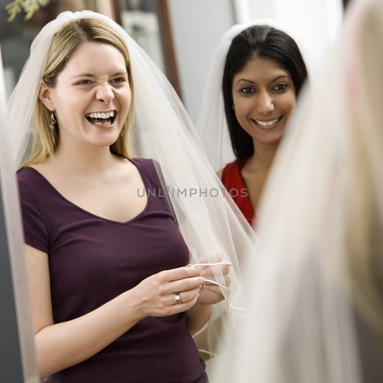 Indian woman and Caucasian woman trying on veils and looking in mirror.