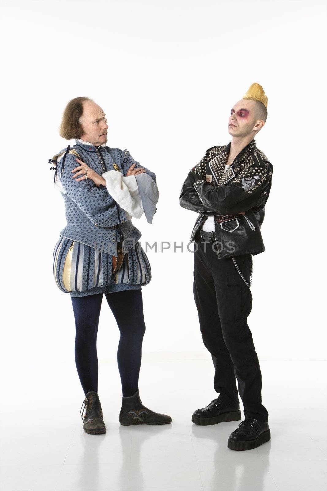 William Shakespeare in period clothing and gothic punk young man standing face to face with arms crossed.