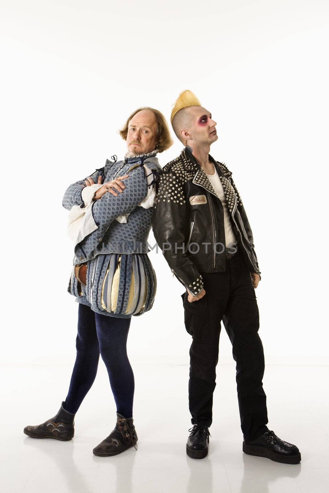 William Shakespeare in period clothing and gothic punk young man standing back to back with arms crossed.