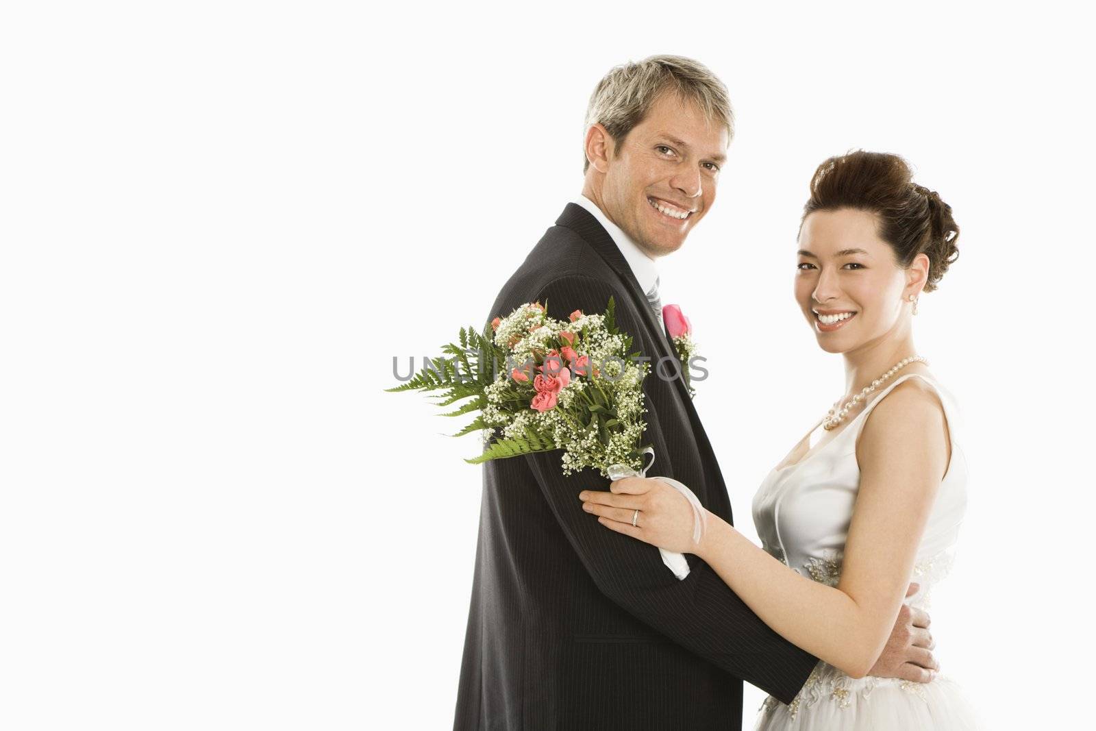 Portrait of Caucasian groom and Asian bride embracing.