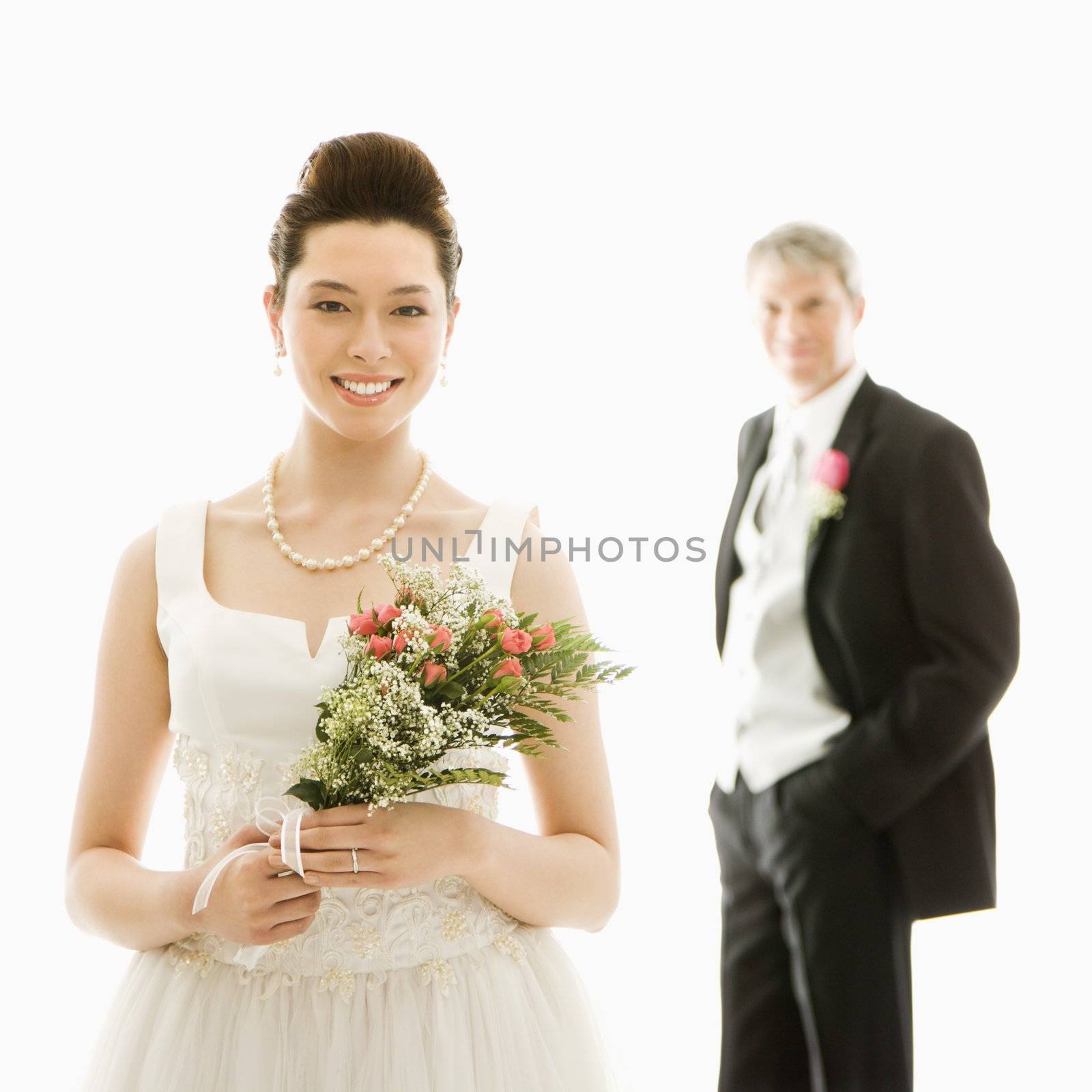 Portrait of Asian bride in foreground and Caucasian groom in background.