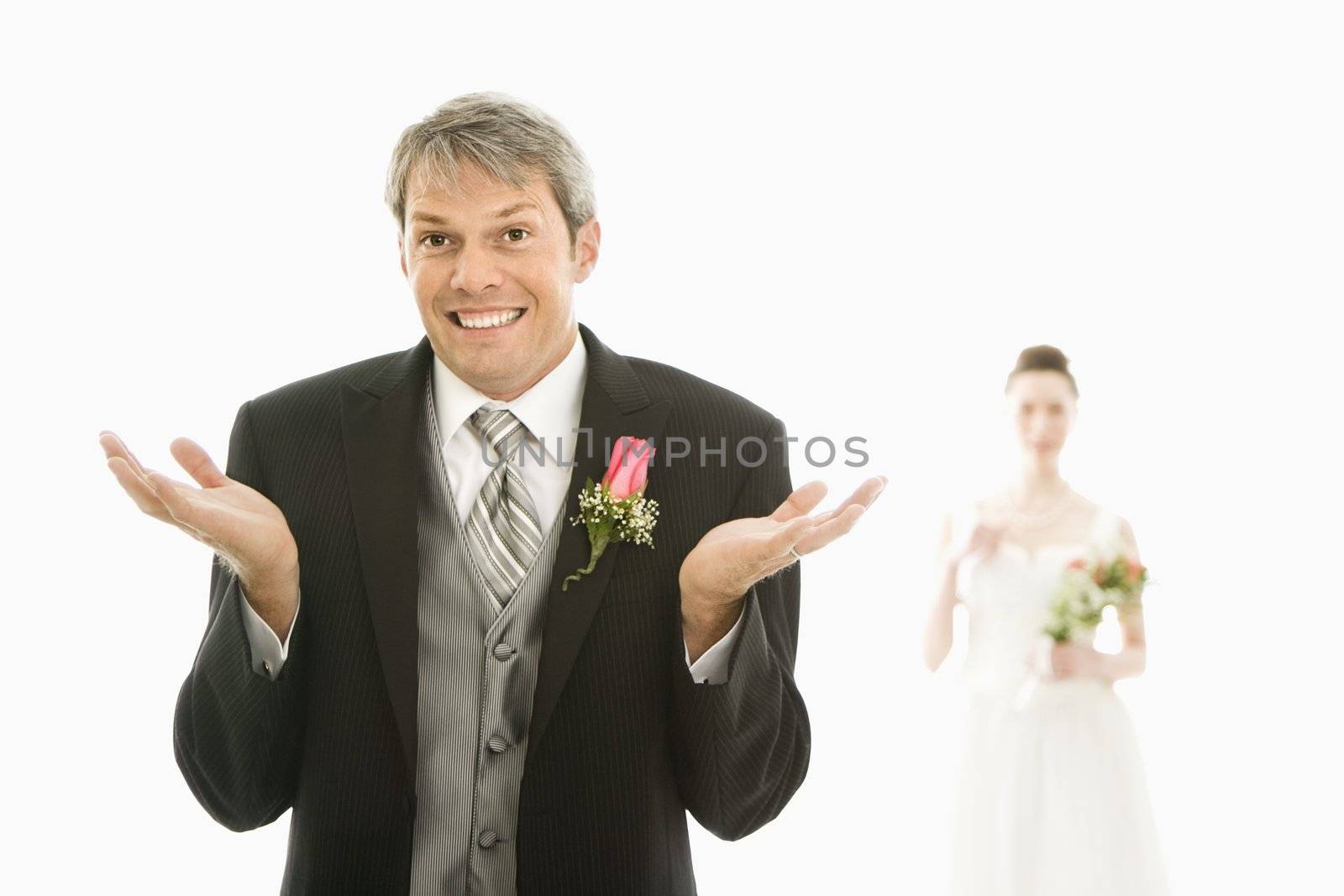 Caucasian groom in foreground with hands raised in air and Asian bride in background.