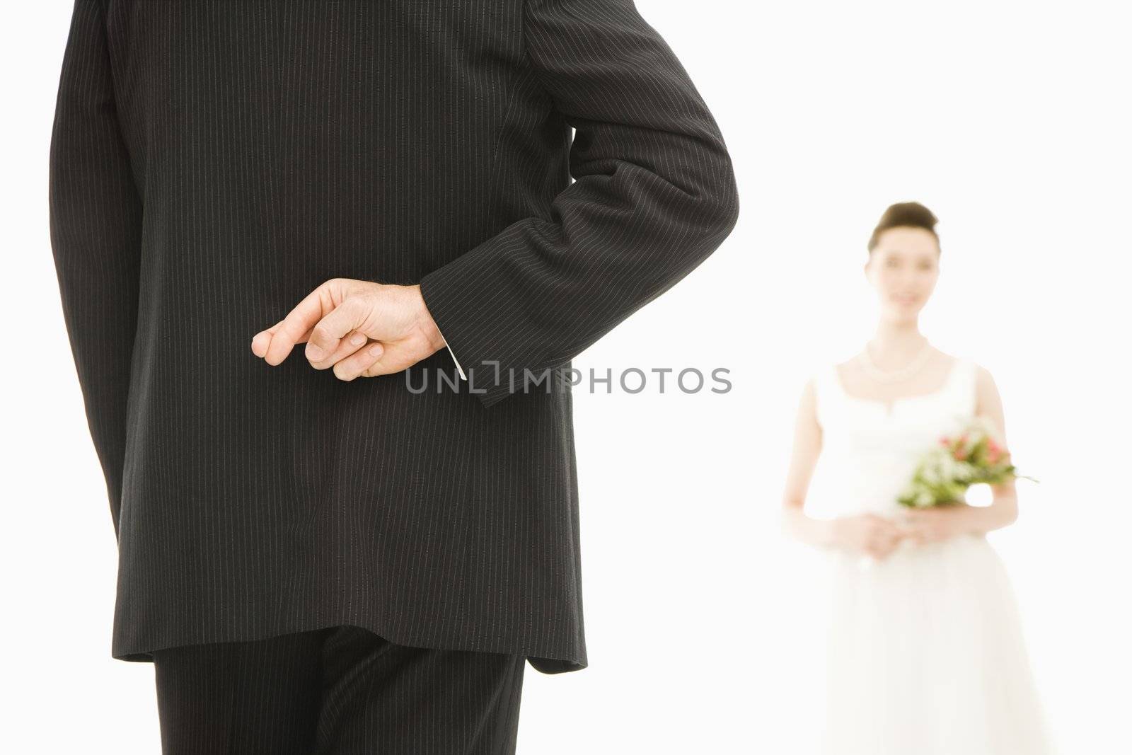 Back of groom with his fingers crossed and Asian bride in background.