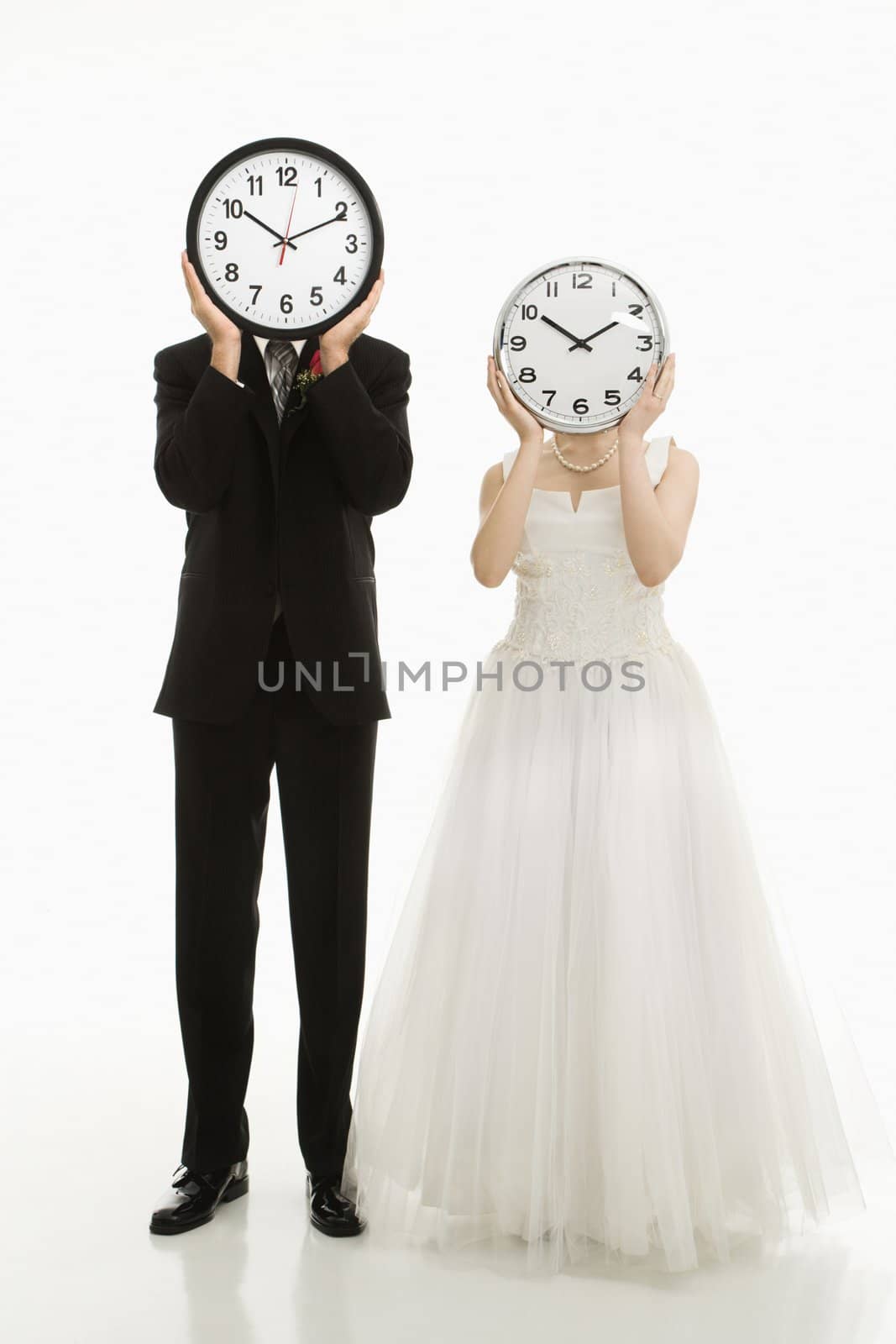 Portrait of Caucasian groom and Asian bride with clocks covering their faces.