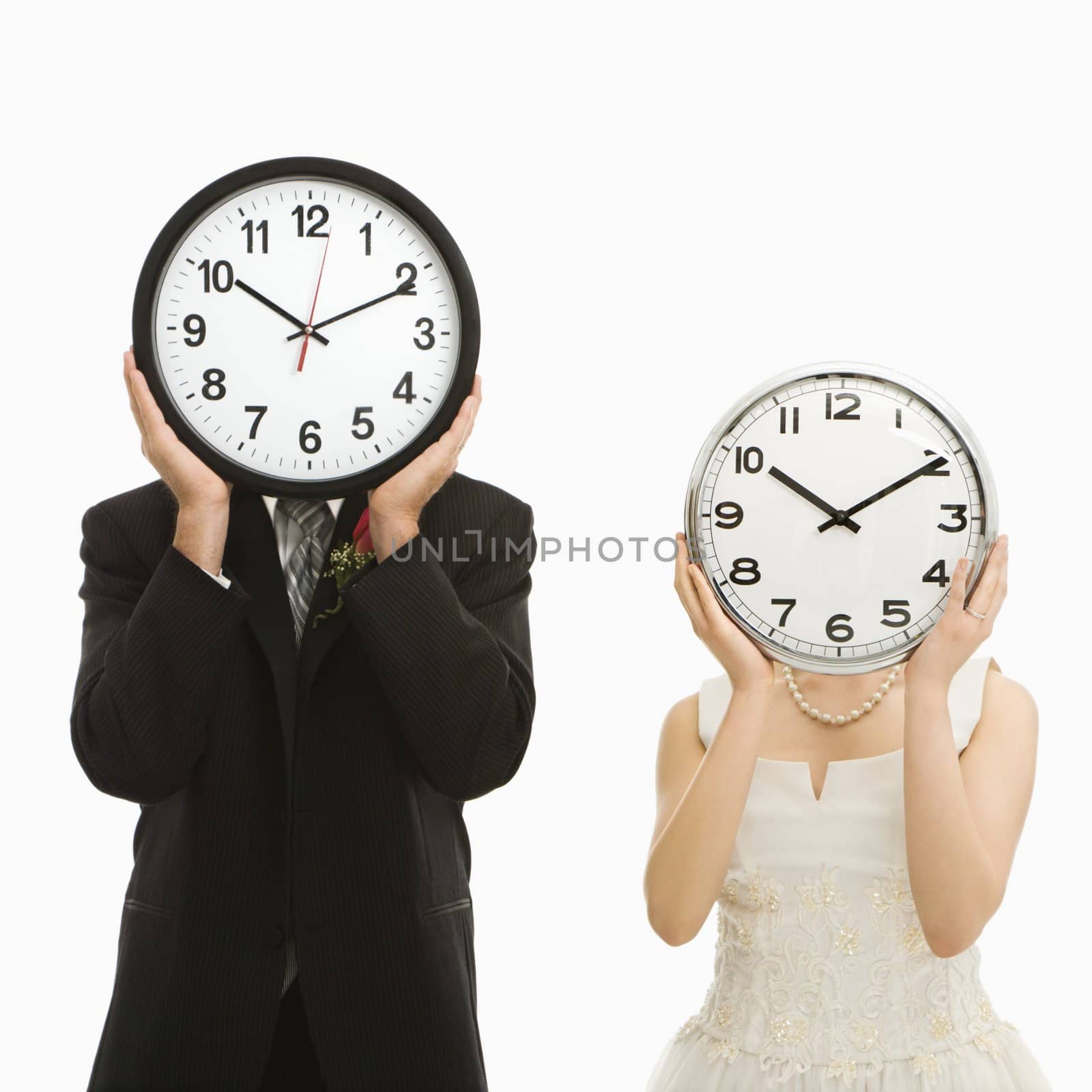 Portrait of Caucasian groom and Asian bride with clocks covering their faces.