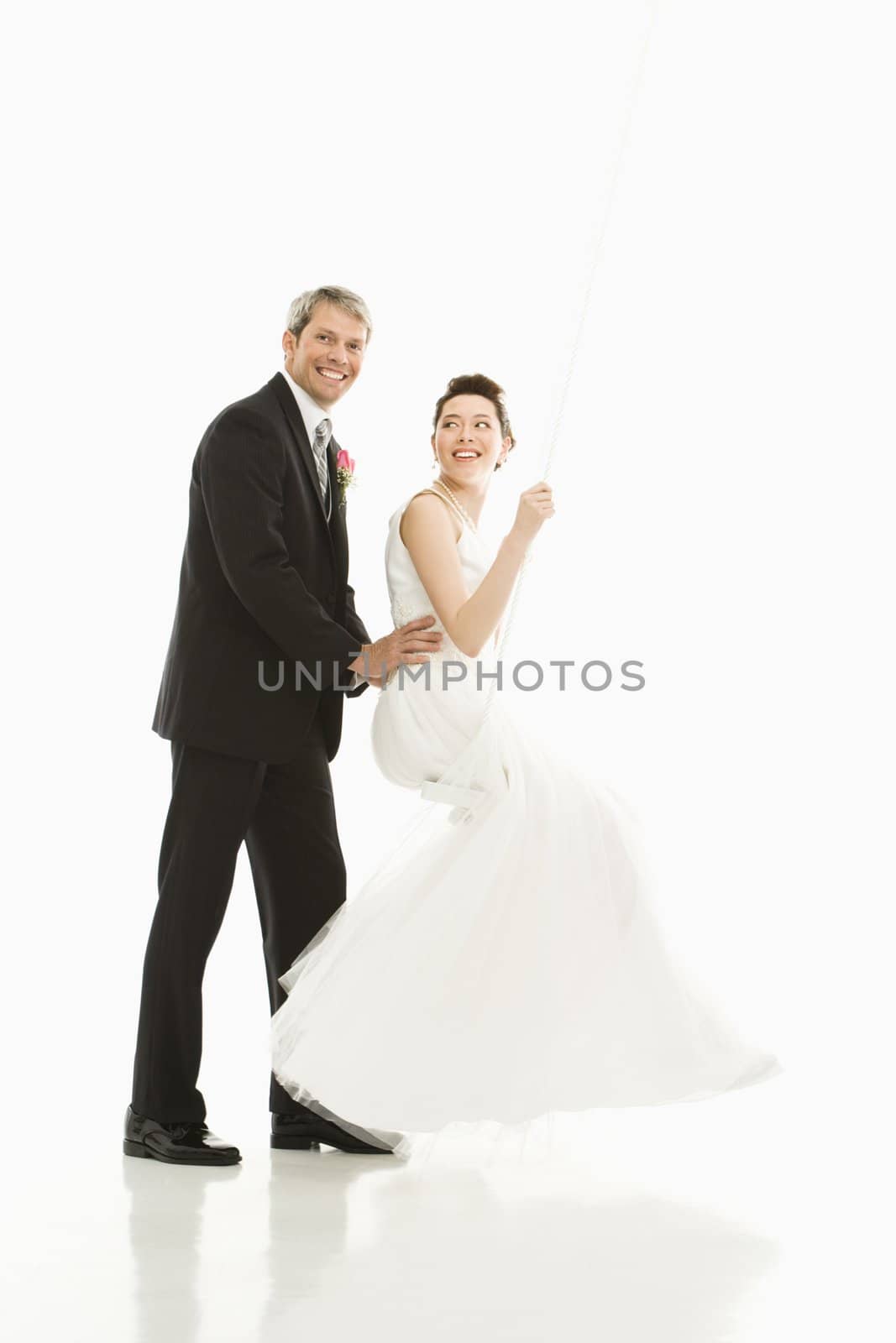 Portrait of Caucasian groom pushing Asian bride in swing.