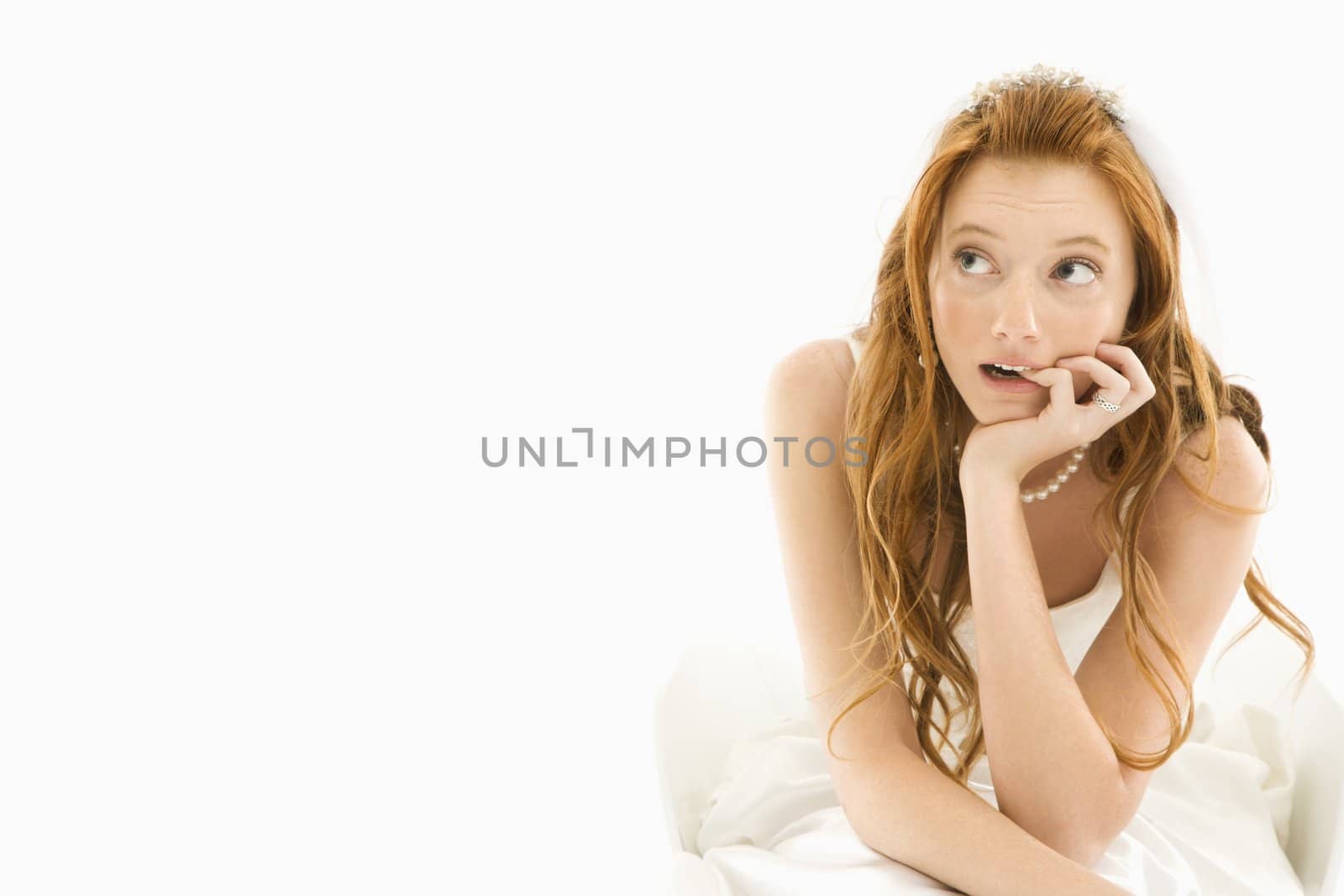 Portrait of sitting Caucasian bride biting her finger and looking off to the side.